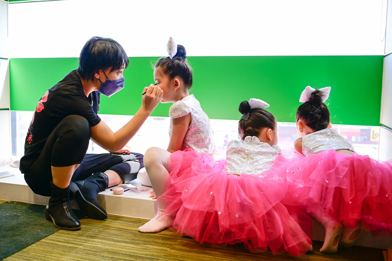 ピンクのチュチュを着た女の子にメイクをするスタッフ